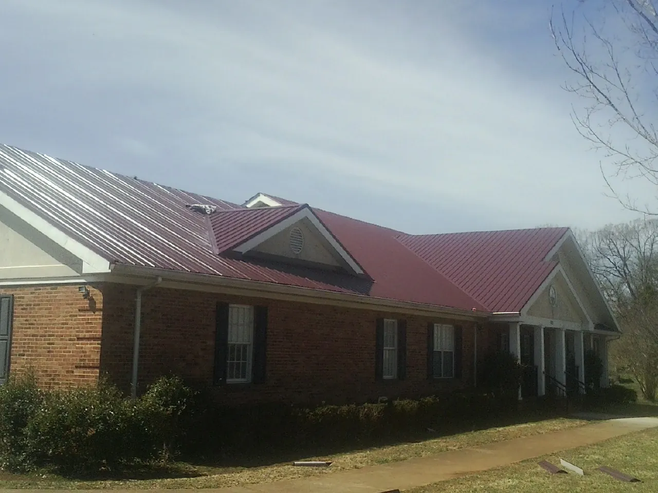 Red metal roof with gabled entries on a long brick building, from a Hail Damage Roof Repair job in Portage