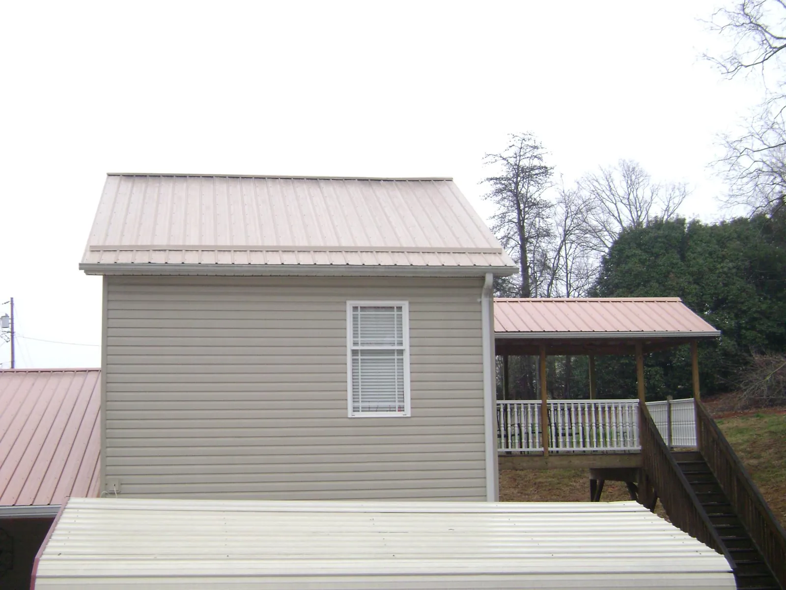 Tan metal roofs on a two story addition and attached porch, from a Roof Replacement job in Portage